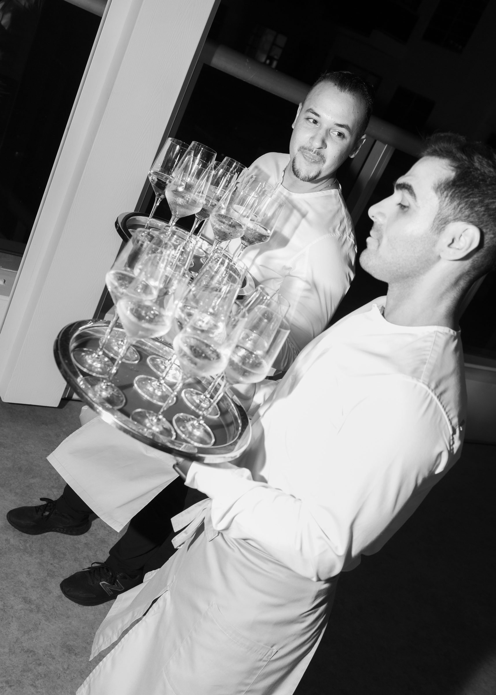 Black and white moment of service staff carrying a tray of coupe glasses at a We Are Ona dinner, photographed by Alicia Valdez